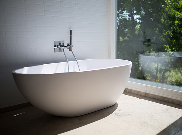 contemporary white bathtub next to white brick on marble slab next to large glass window